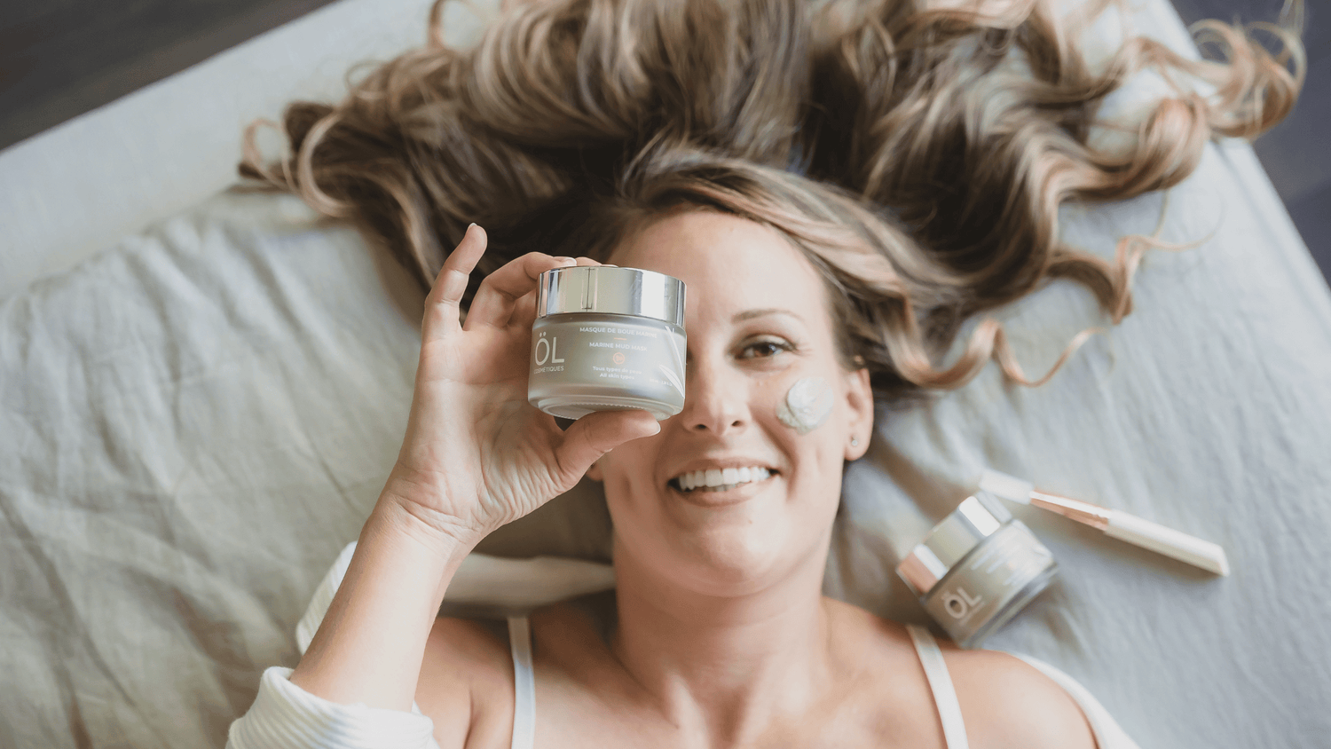 Femme allongée sur un lit tenant un peau de masque de boue marine devant son visage